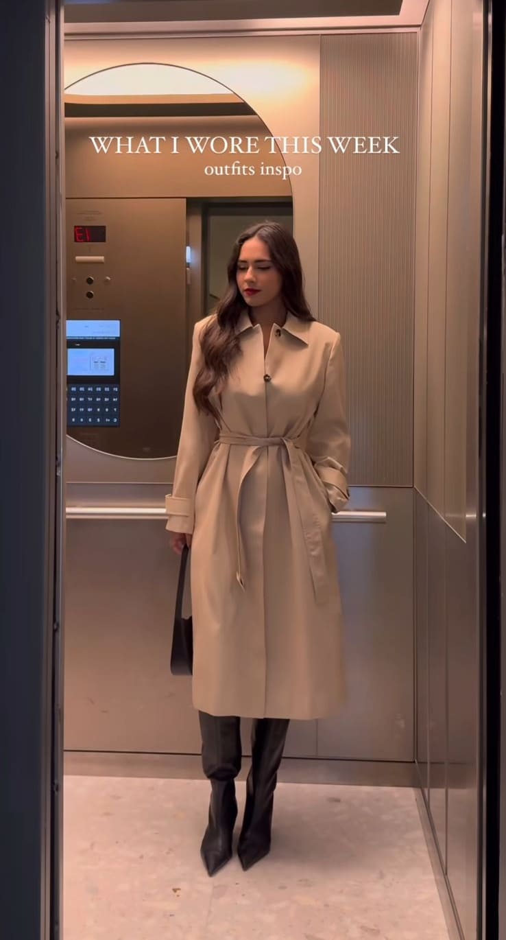 Beige belted trench coat with black knee-high boots in a mirrored elevator